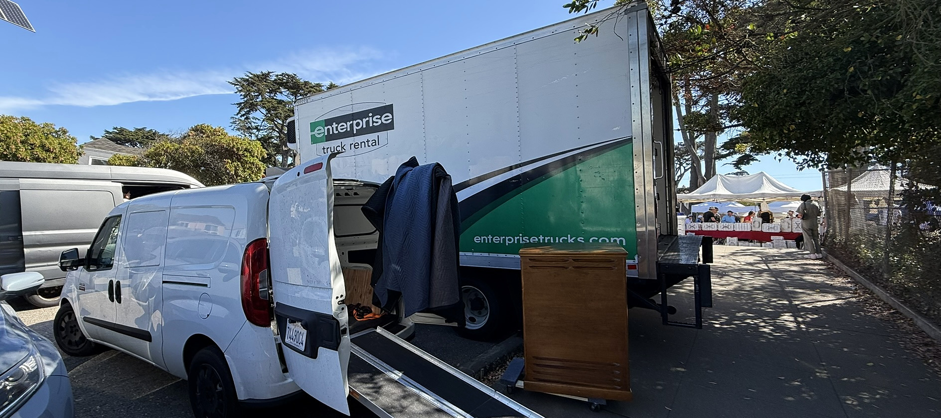 White cargo van and box truck during a Hammond organ load-in, with a wooden organ cabinet beside the ramp